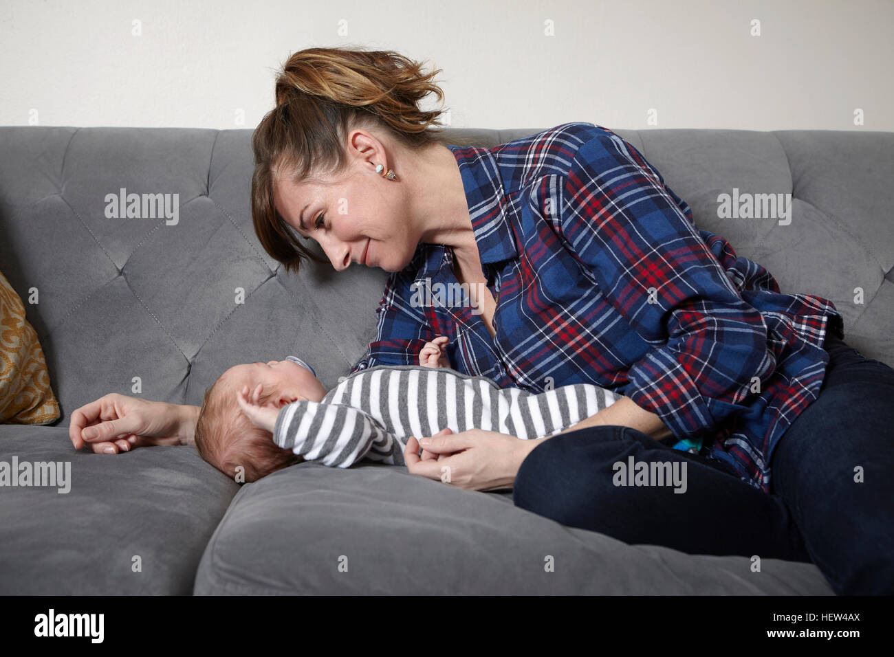 Madre sul divano guardando sleeping baby boy, sorridente Foto Stock