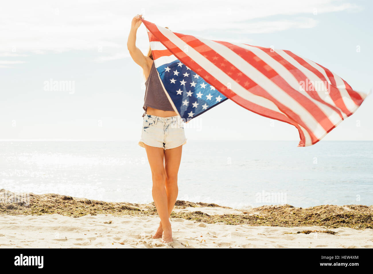 Donna sulla spiaggia a braccia alzate tenendo bandiera americana Foto Stock
