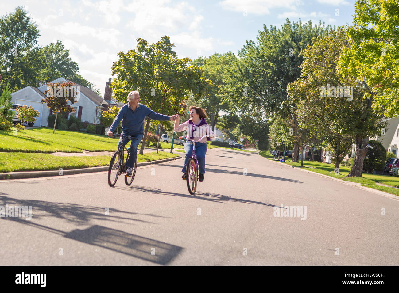 Romantico coppia senior holding hands escursioni in bicicletta lungo la strada suburbana Foto Stock