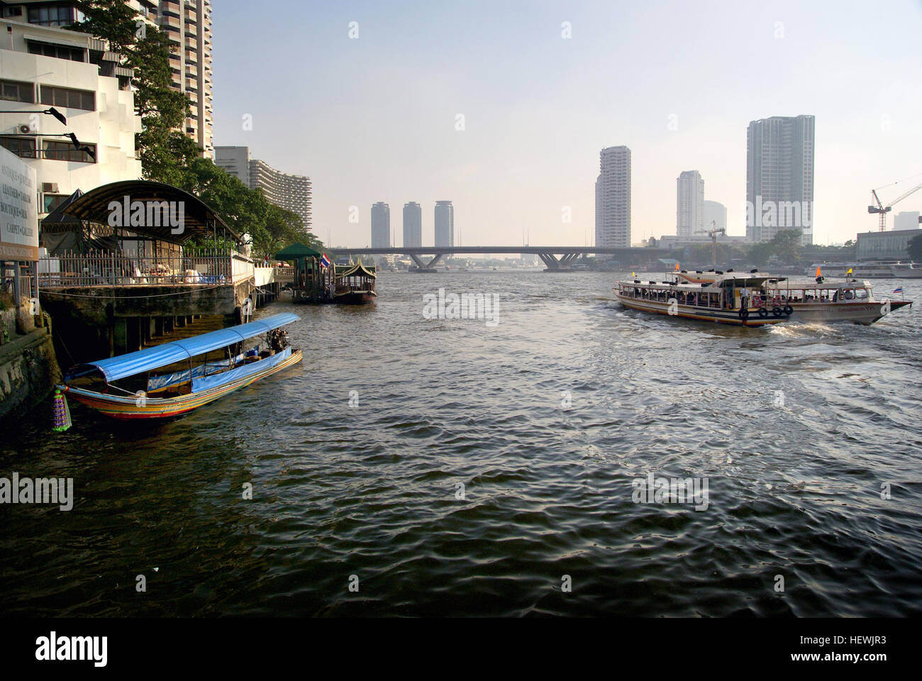 Il fiume Chao Phraya a Bangkok è una via d'acqua vitale, storicamente conosciuta come il "fiume dei Re". Funge da linfa vitale della città, con traghetti, barche da carico e attività ricreative in acqua. Il fiume è fiancheggiato da baracche di legno e offre un ambiente pittoresco per la vita quotidiana a Bangkok. Foto Stock