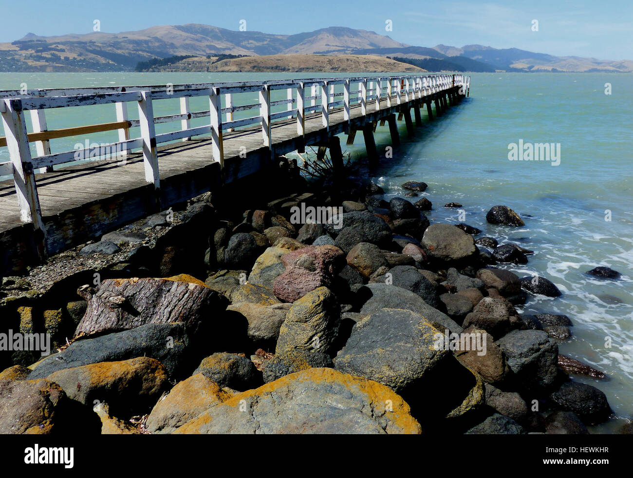 Questa vista panoramica di Rapaki, situata a Canterbury, nuova Zelanda, offre un paesaggio pittoresco con una baia, un molo e una piccola chiesa. L'insediamento è conosciuto per il suo ambiente tranquillo, ideale per una visita tranquilla. Il porto circostante aggiunge fascino alla zona. Foto Stock