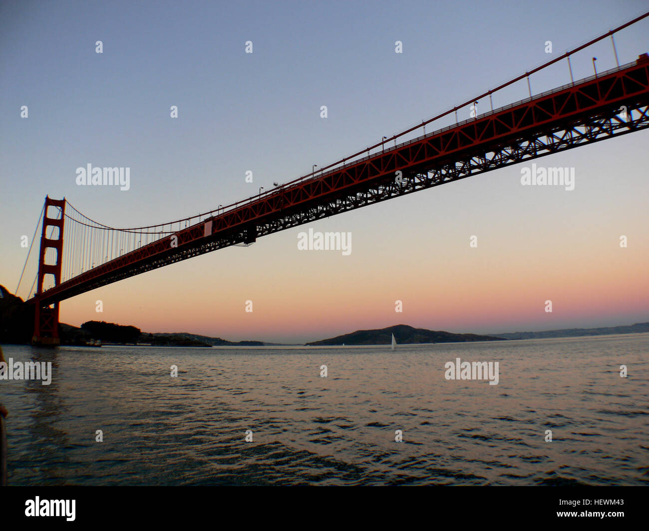Il Golden Gate Bridge di San Francisco viene mostrato al tramonto, con la sua iconica tonalità rosso-arancione che contrasta con la luce del giorno che svanisce. L'immagine mette in risalto uno dei monumenti più riconoscibili al mondo, noto per la sua meraviglia ingegneristica e la splendida posizione nella Bay area. Foto Stock