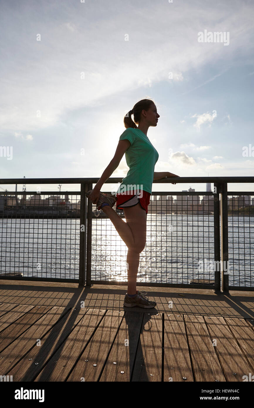Vista laterale della donna lo stiramento della gamba sul molo, Manhattan, New York, Stati Uniti d'America Foto Stock