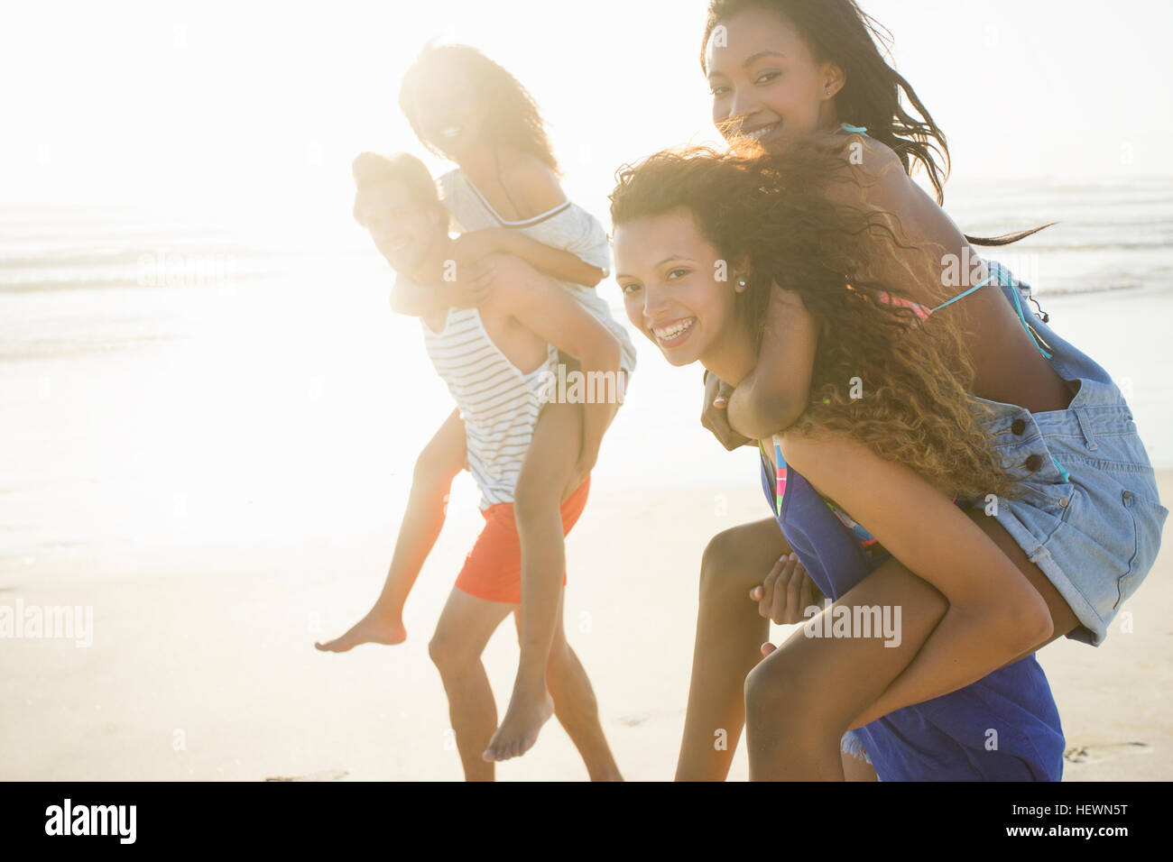 Giovane uomo e donna piggybacking amici in gara sulla spiaggia, Cape Town, Sud Africa Foto Stock