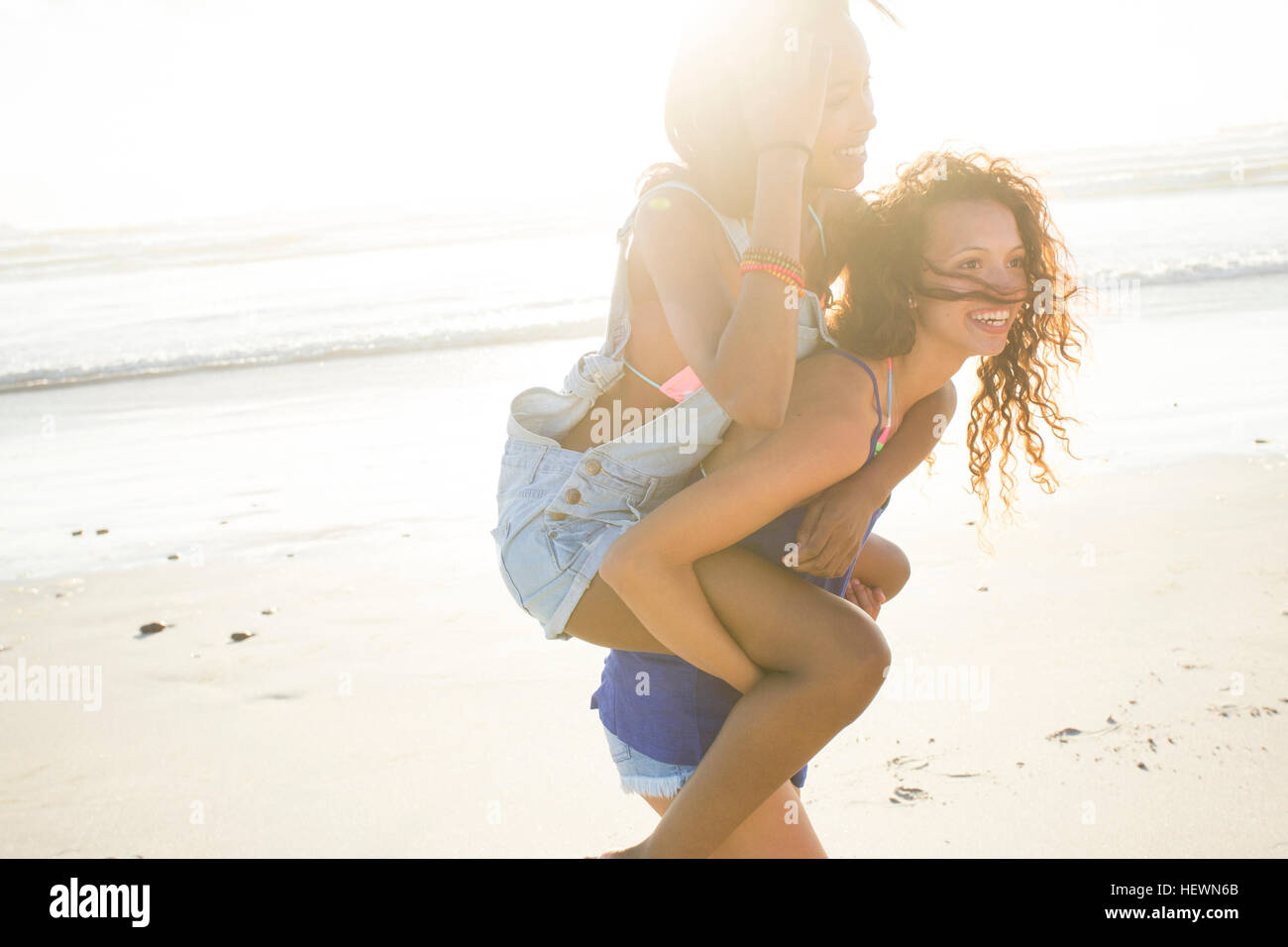 Giovane donna femmina piggybacking amico sulla spiaggia, Cape Town, Sud Africa Foto Stock