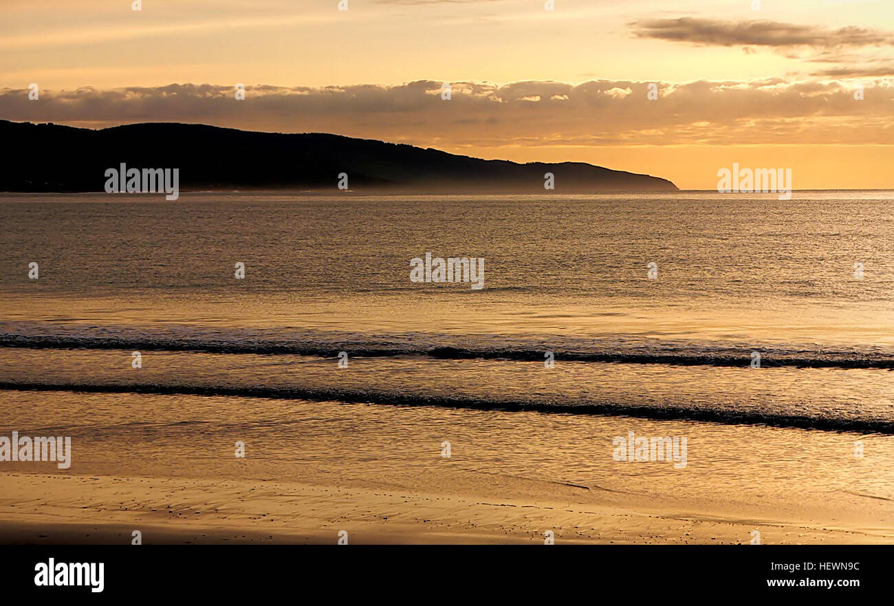 Questa immagine cattura la spettacolare costa lungo la Great Ocean Road in Australia, mostrando spiagge sabbiose, scogliere e il surf. La foto evidenzia la bellezza naturale della regione, con un ponte visibile in lontananza. La Great Ocean Road è conosciuta per le sue viste mozzafiato e le diverse caratteristiche costiere. Foto Stock