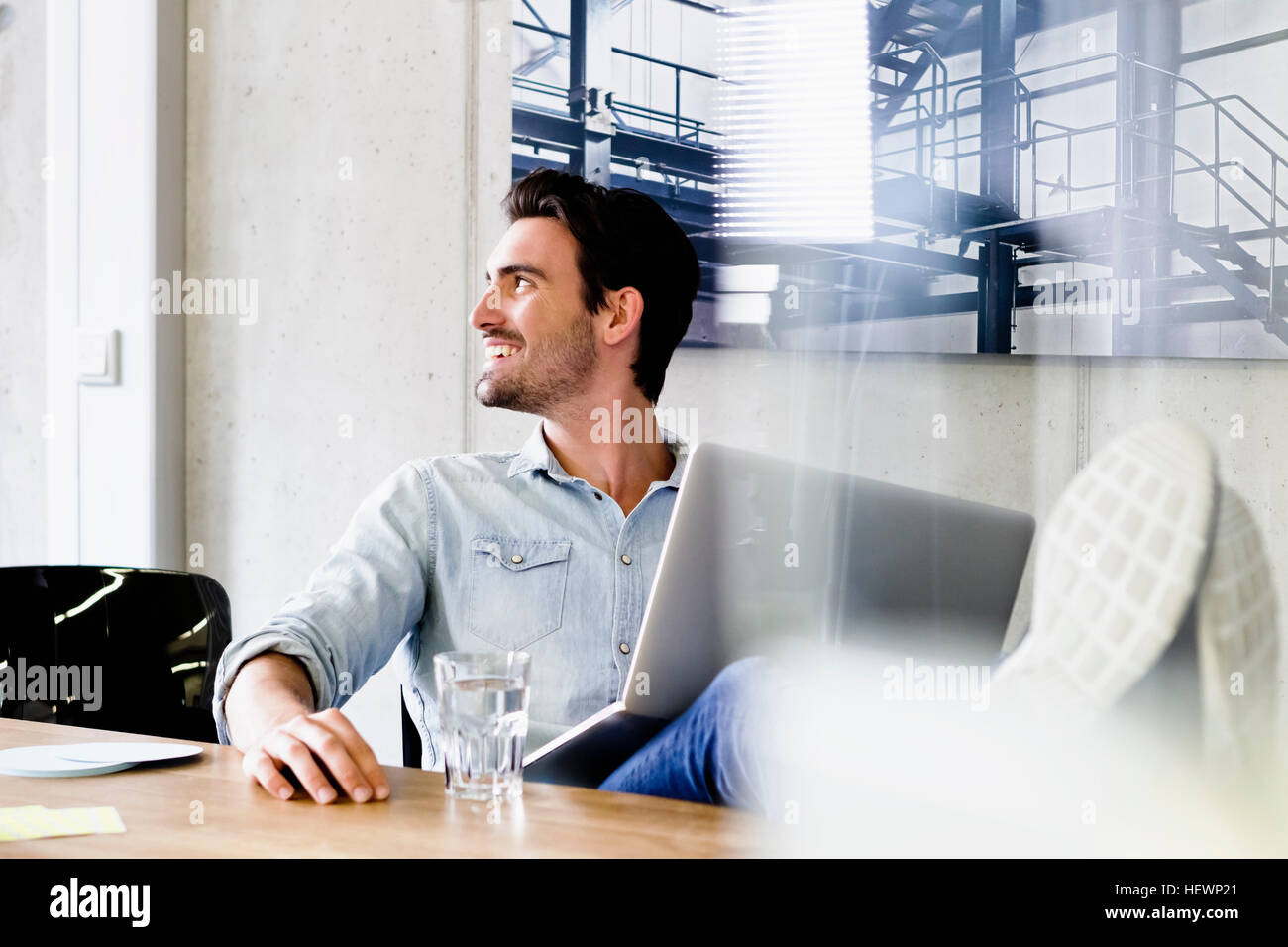 Business man in office piedi sulla scrivania, utilizzando laptop che guarda lontano sorridente Foto Stock