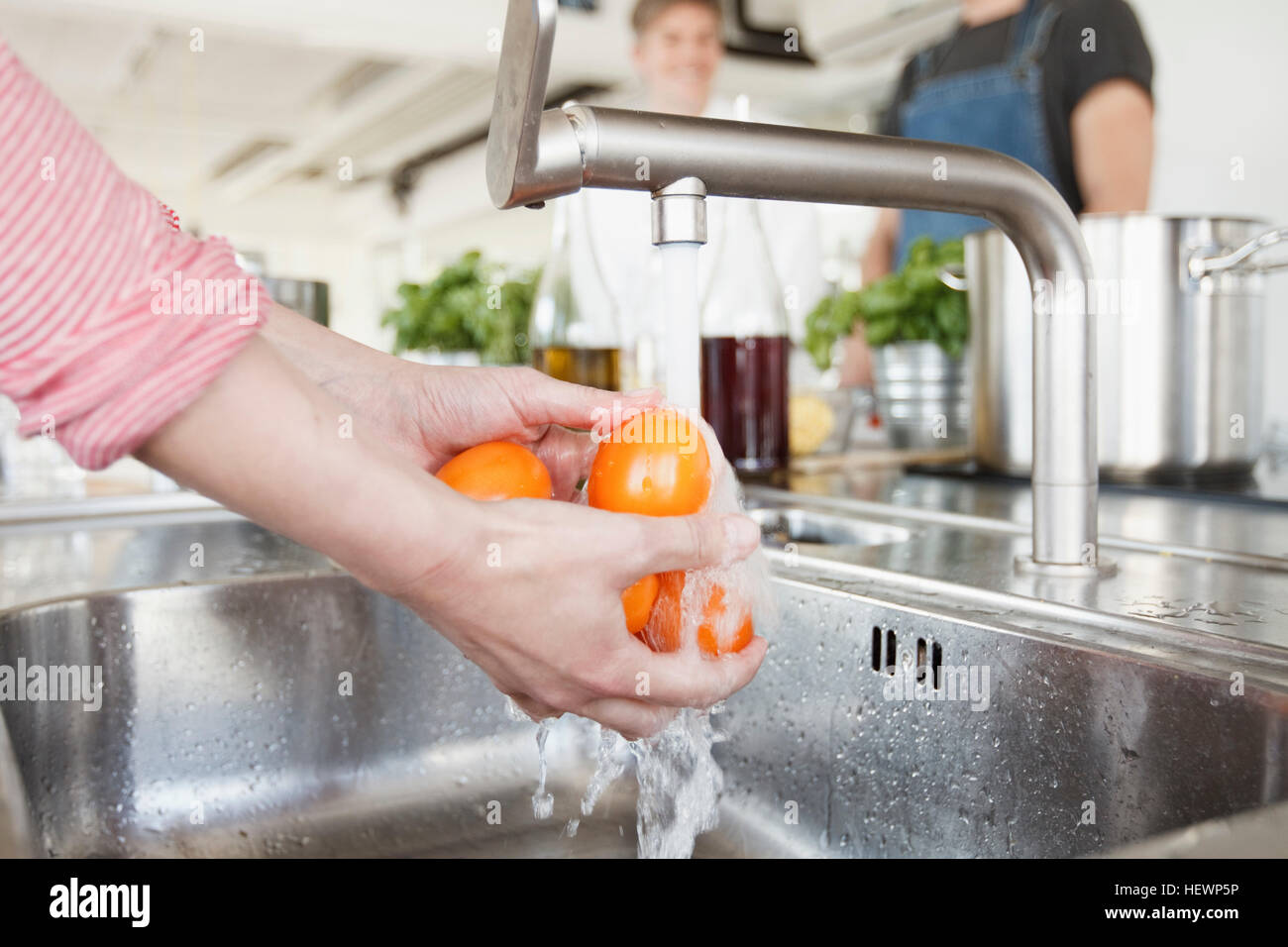Vista ritagliata della donna di lavaggio mani pomodori sotto tocca Foto Stock