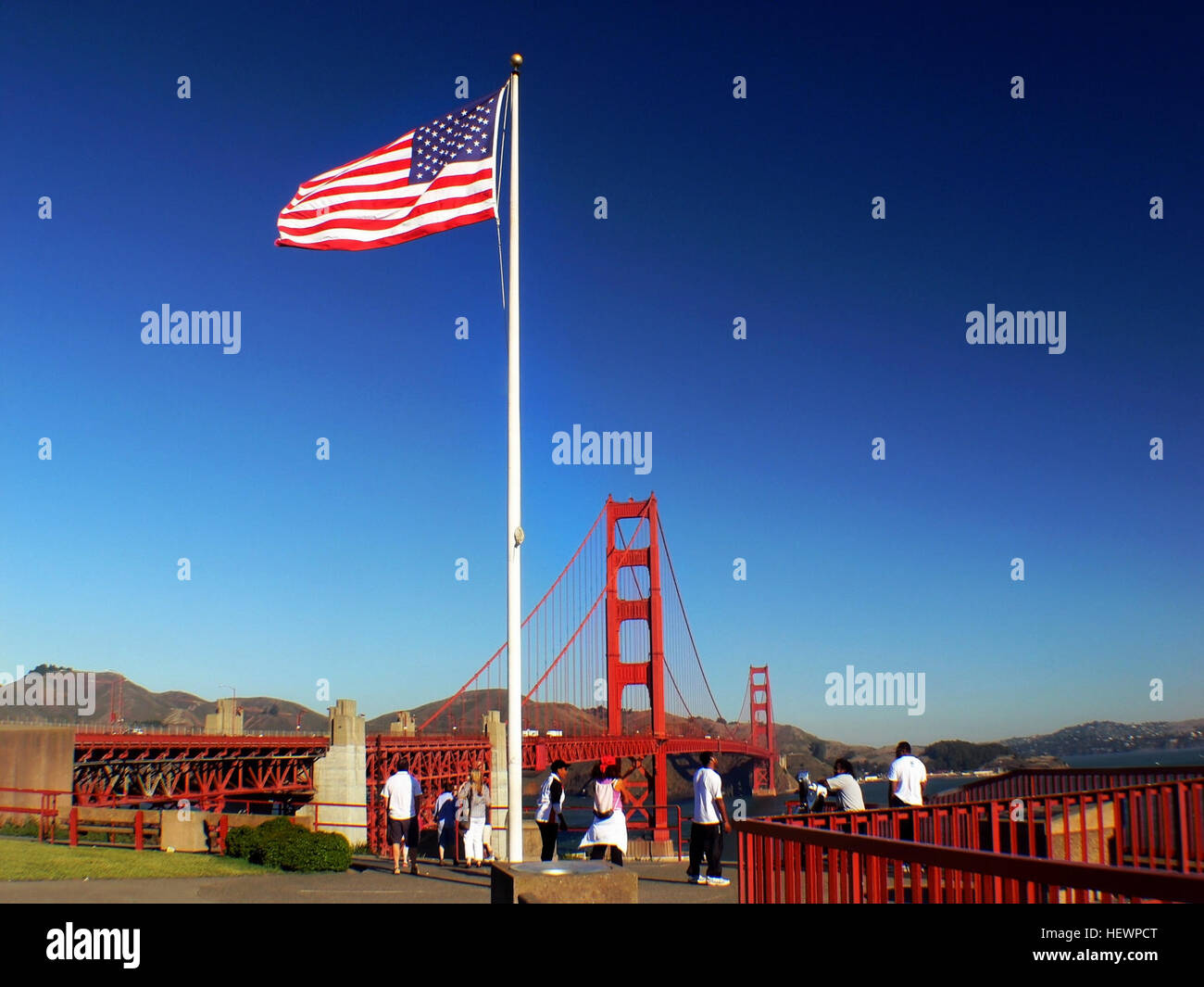 Questa immagine presenta l'iconico Golden Gate Bridge e il vicino traghetto, con vedute della Old Glory, la bandiera americana, in primo piano. Fa parte di una crociera nel porto di San Francisco che offre un tour al tramonto per visite turistiche, mostrando i famosi punti di riferimento della città. Foto Stock