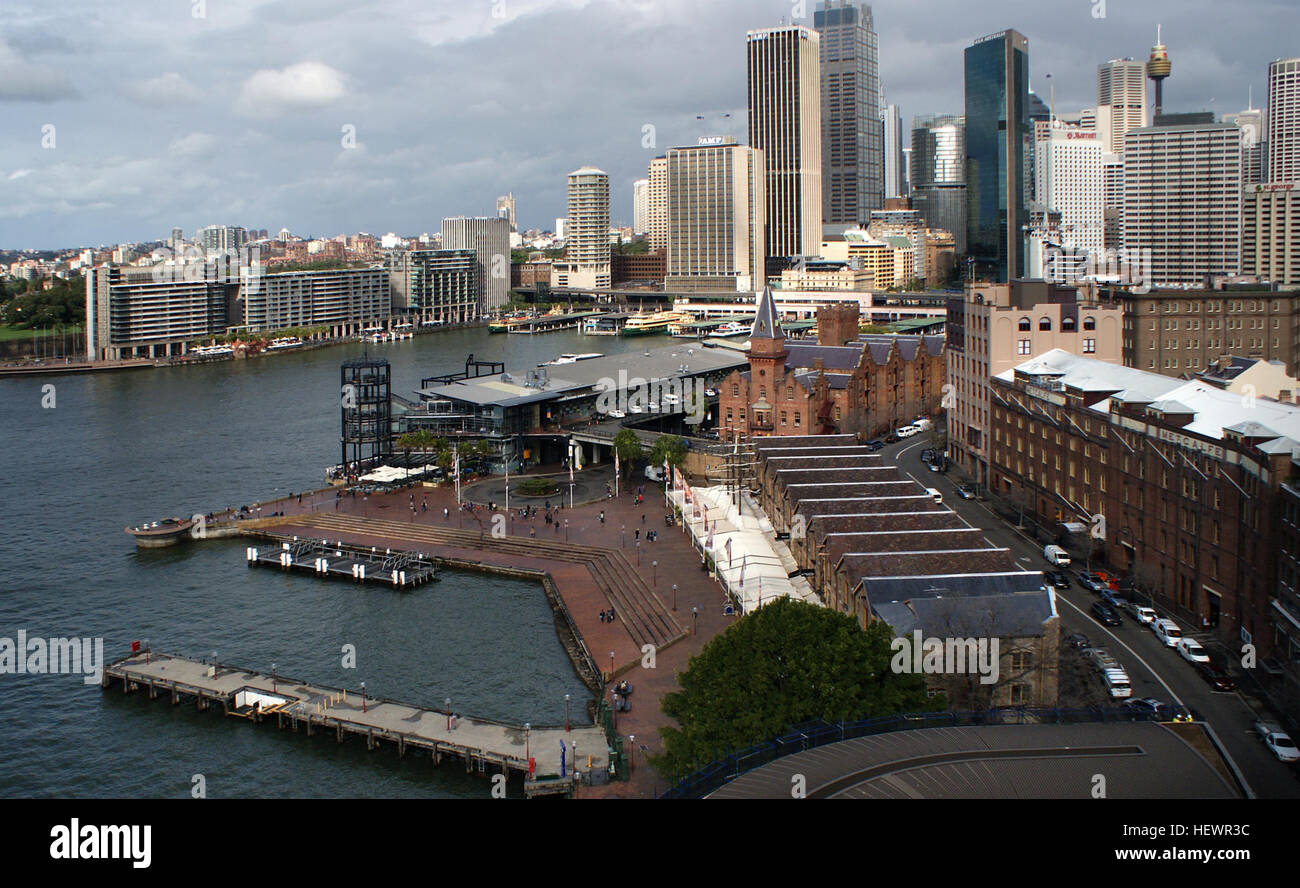 Questa fotografia cattura Circular Quay a Sydney, con traghetti come la Manly Ferries che attraversano Port Jackson. Il Sydney Harbour Bridge e The Rocks sono visibili, evidenziando i simboli del lungomare di Sydney. Foto Stock
