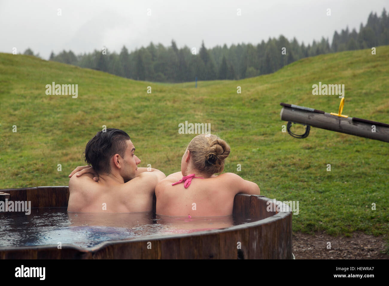 Vista posteriore della coppia giovane rilassante nelle zone rurali la vasca calda Sattelbergalm, Tirolo, Austria Foto Stock