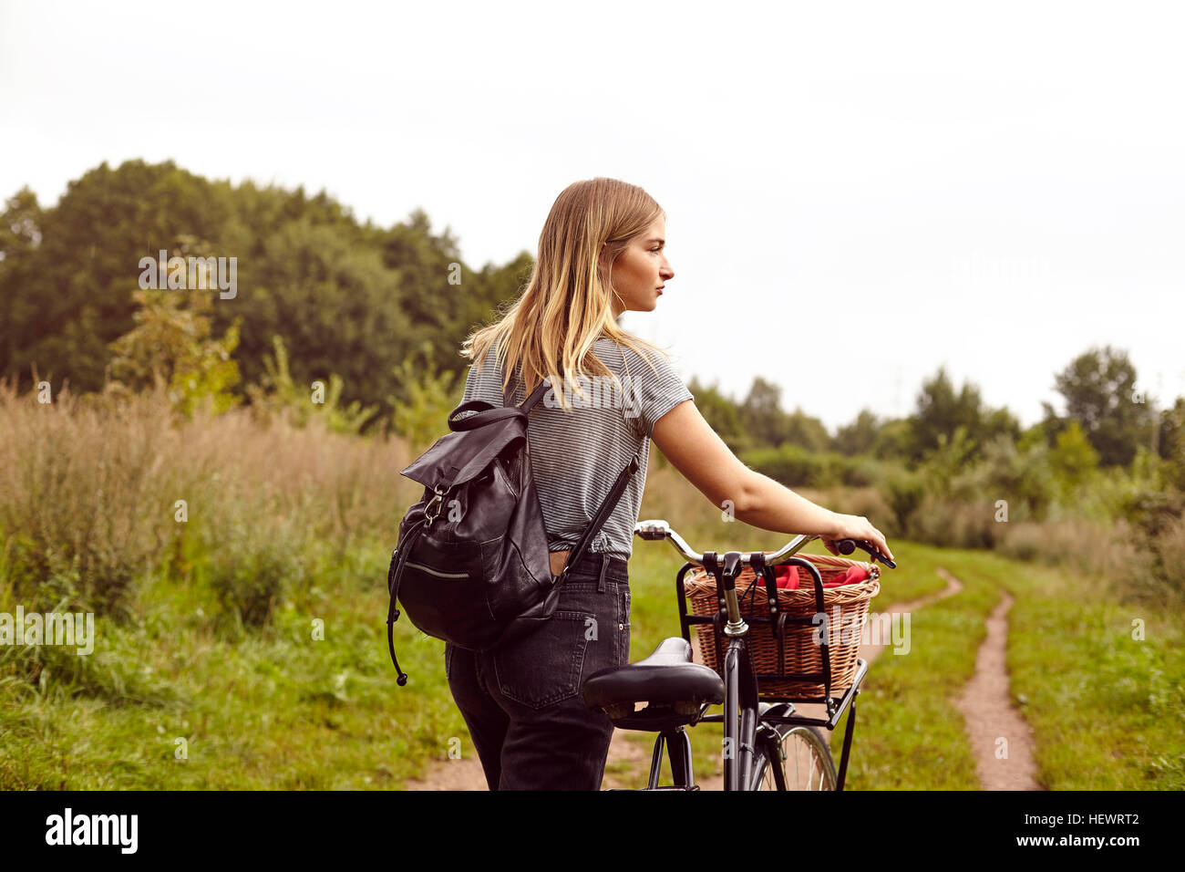 Giovane donna con la bicicletta guardando sopra la sua spalla da rurale traccia di sporco Foto Stock