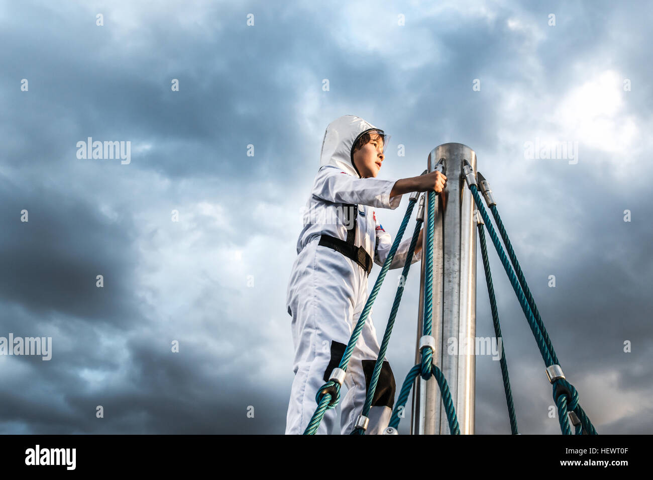 Ragazzo in costume da astronauta guardando dalla parte superiore del telaio di arrampicata contro il cielo drammatico Foto Stock