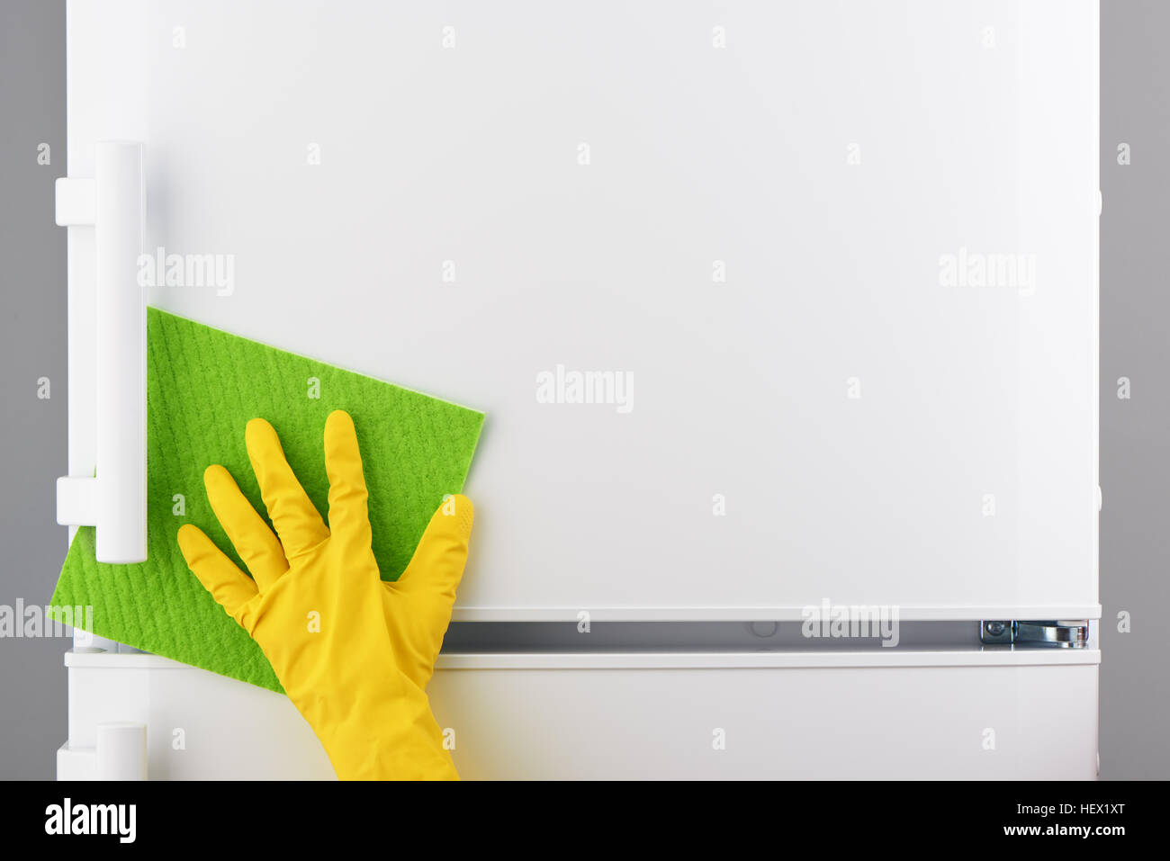 Mano di donna gomma gialla di guanto protettivo pulizia frigorifero bianco con panno verde su sfondo grigio Foto Stock