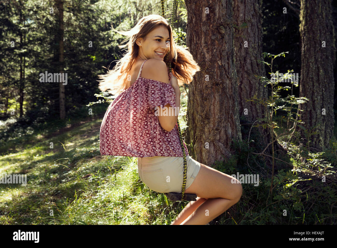 Giovane donna basculante in foresta swing, Sattelbergalm, Tirolo, Austria Foto Stock