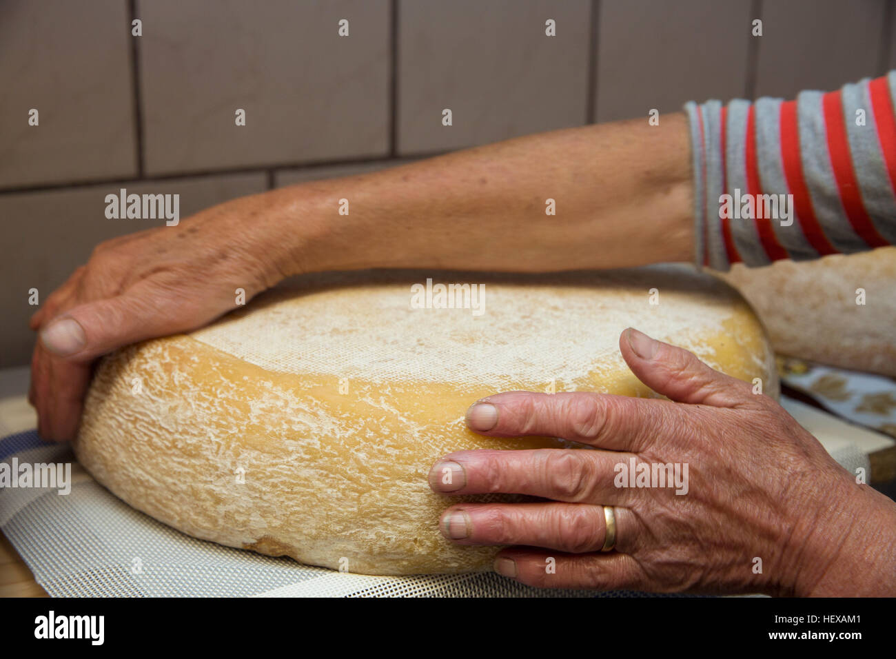 Mani femminili di produttore di latte girando tutto il formaggio in cucina, Sattelbergalm, Tirolo, Austria Foto Stock