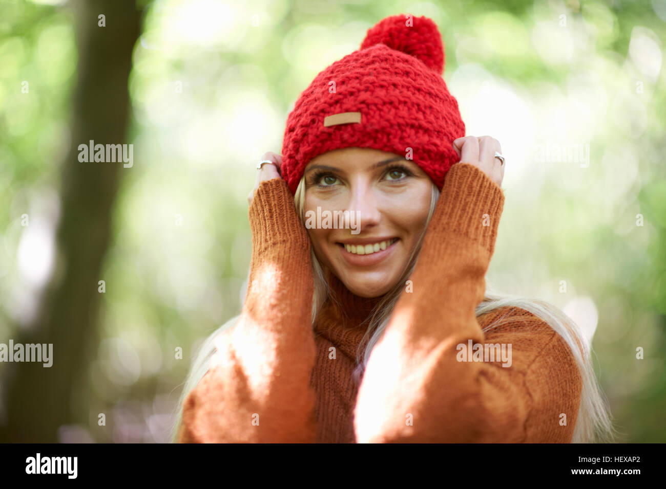Ritratto di donna che indossa knit hat, le mani sulla testa che guarda lontano Foto Stock