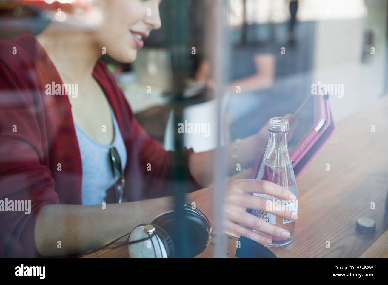 Giovane donna seduta al cafe, tenendo in mano una bottiglia di acqua minerale, utilizzando tavoletta digitale Foto Stock
