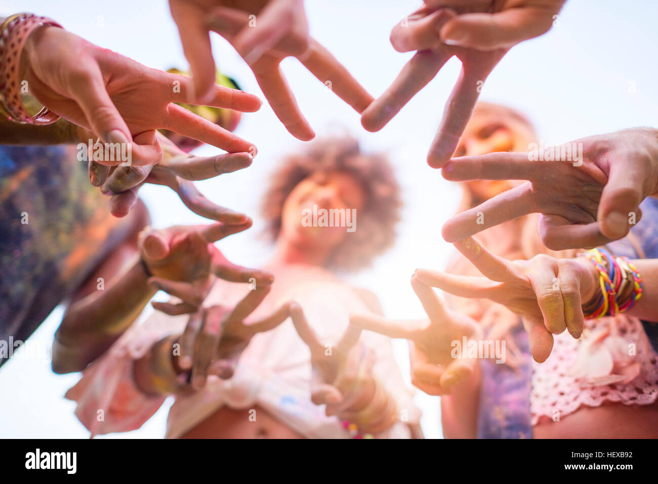 Gruppo di amici al festival, coperto di polvere colorata vernice, collegando le dita con il segno di pace e a basso angolo di visione Foto Stock