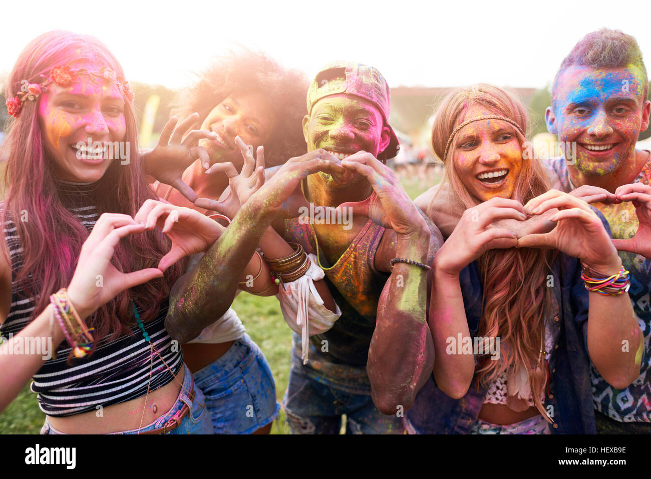 Ritratto di gruppo di amici al festival, coperte in colorate vernice in polvere, rendendo il cuore di forme con le mani Foto Stock