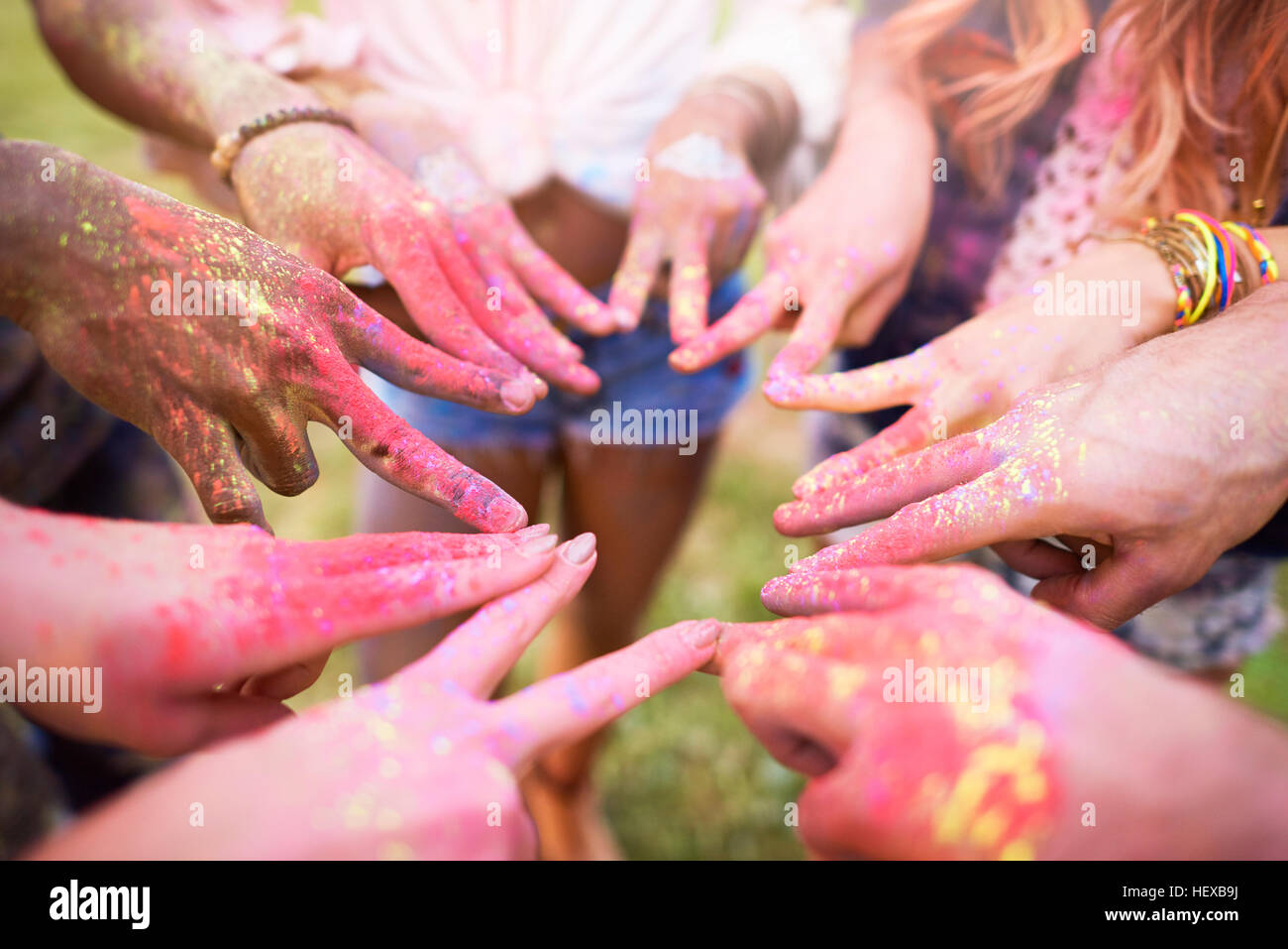 Gruppo di amici al festival, coperto di polvere colorata vernice, collegando le dita con segni di pace, close-up Foto Stock
