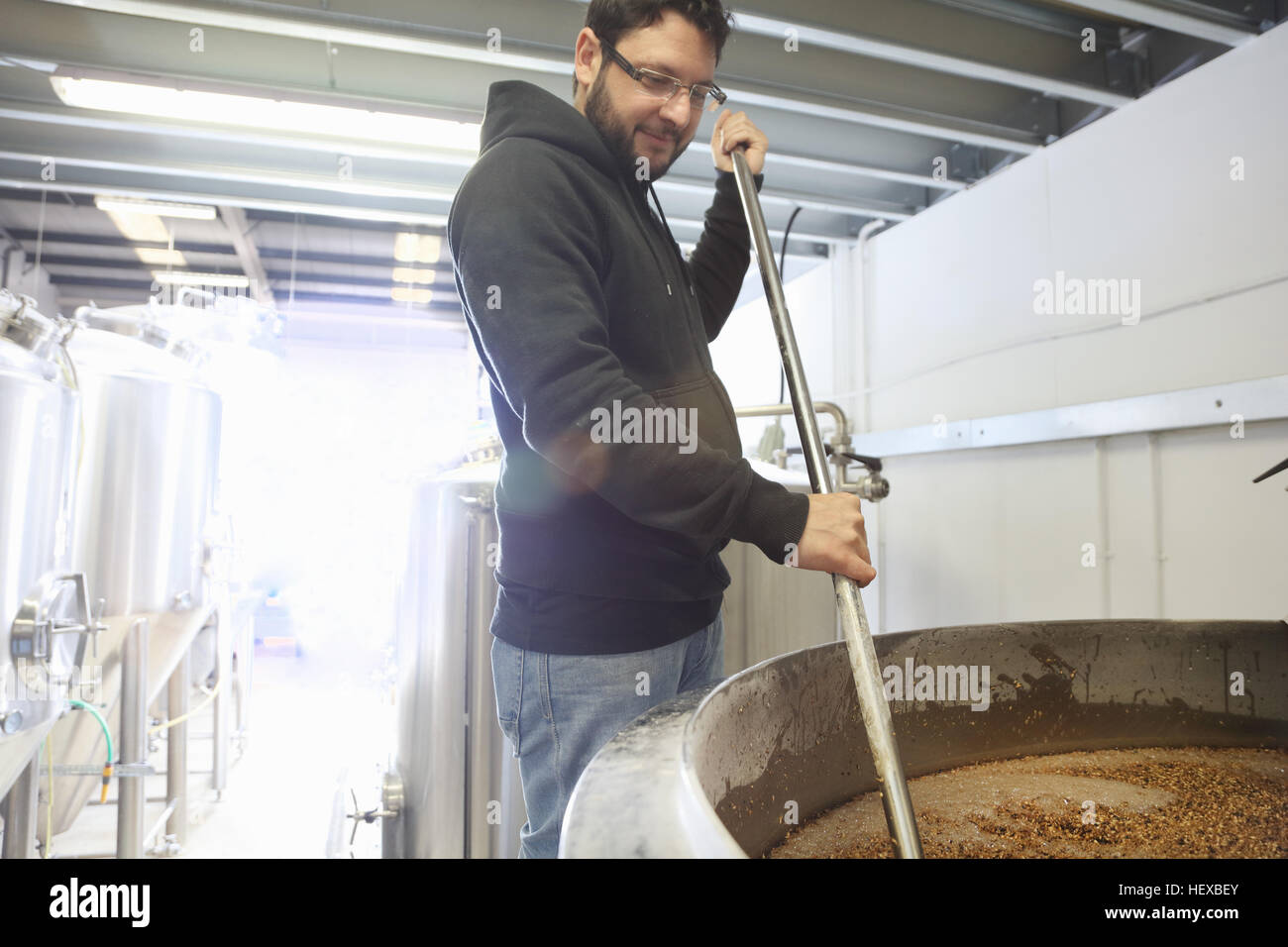 Lavoratore in birreria, la miscelazione di chicchi d'orzo nel serbatoio brew Foto Stock