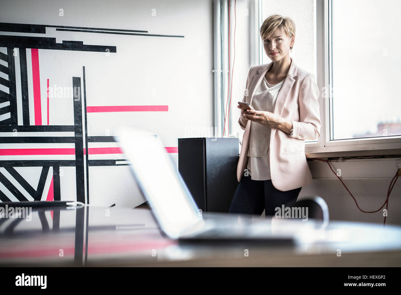 Fiducioso imprenditrice con un telefono cellulare in piedi in un ufficio moderno Foto Stock