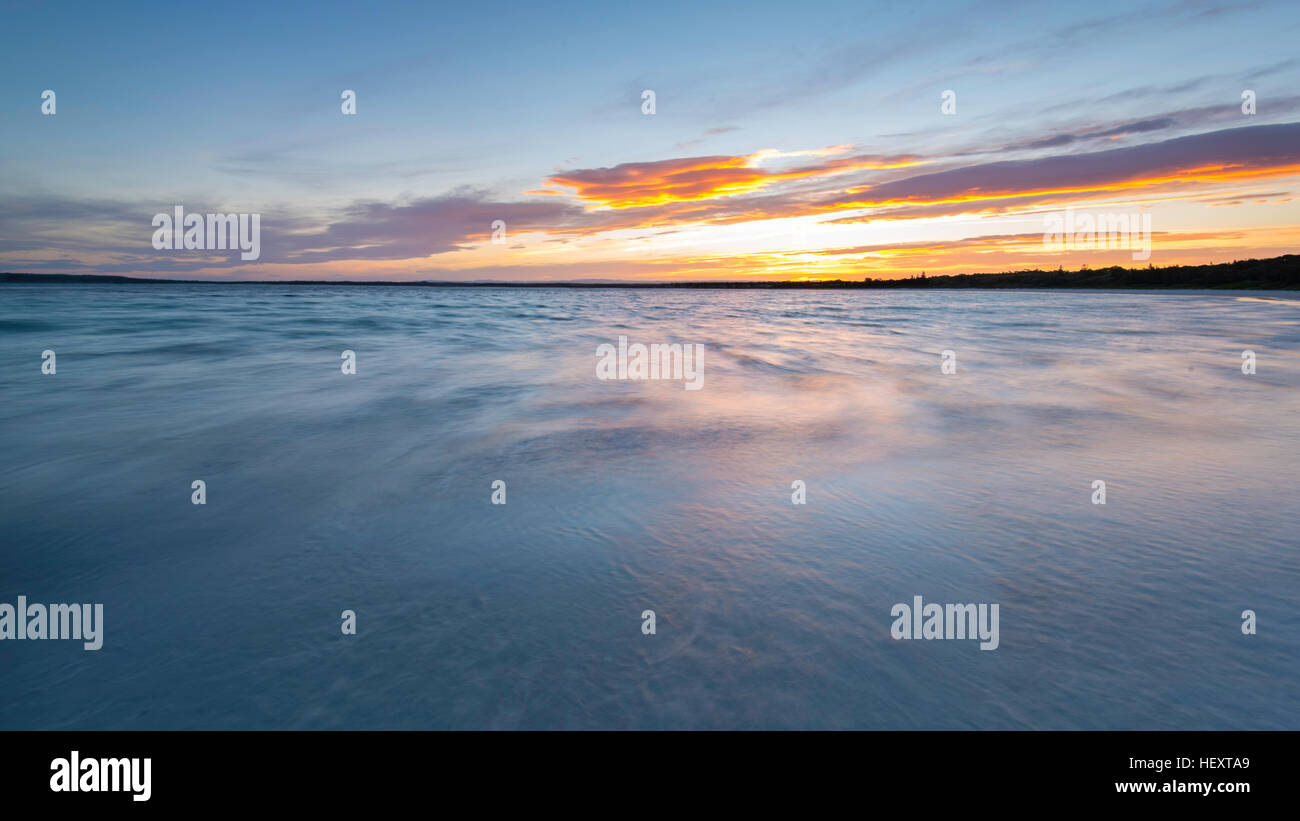 Una vista ampia e tranquilla sull'acqua dell'oceano con distese di terra e sole che si riflette sulle nuvole mentre si affaccia su Callala Bay in NSW, Australia Foto Stock