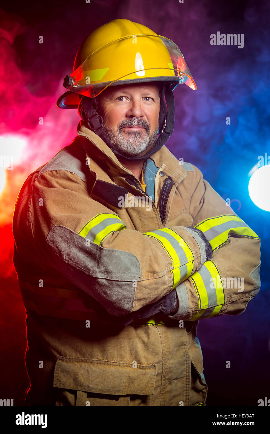 Ritratto di un vigile del fuoco che indossa Fire Fighter scambi e casco. Lo sfondo è di colore rosso e blu fumo e luce. Sono scambi per proteggere Foto Stock