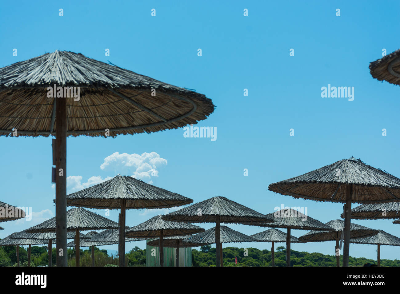 Astratto e concettuale, estate ombrelloni di paglia o di vimini. Con il cielo blu e nuvole bianche su una spiaggia del Mediterraneo. Foto Stock