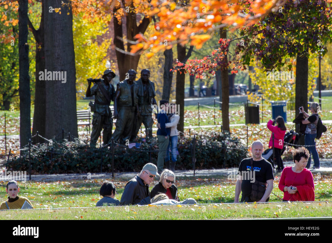 I visitatori in primo piano a piedi in discesa su un pendio la lettura dei nomi dalla parete presso il Memoriale dei Veterani del Vietnam a Washington DC. Foto Stock