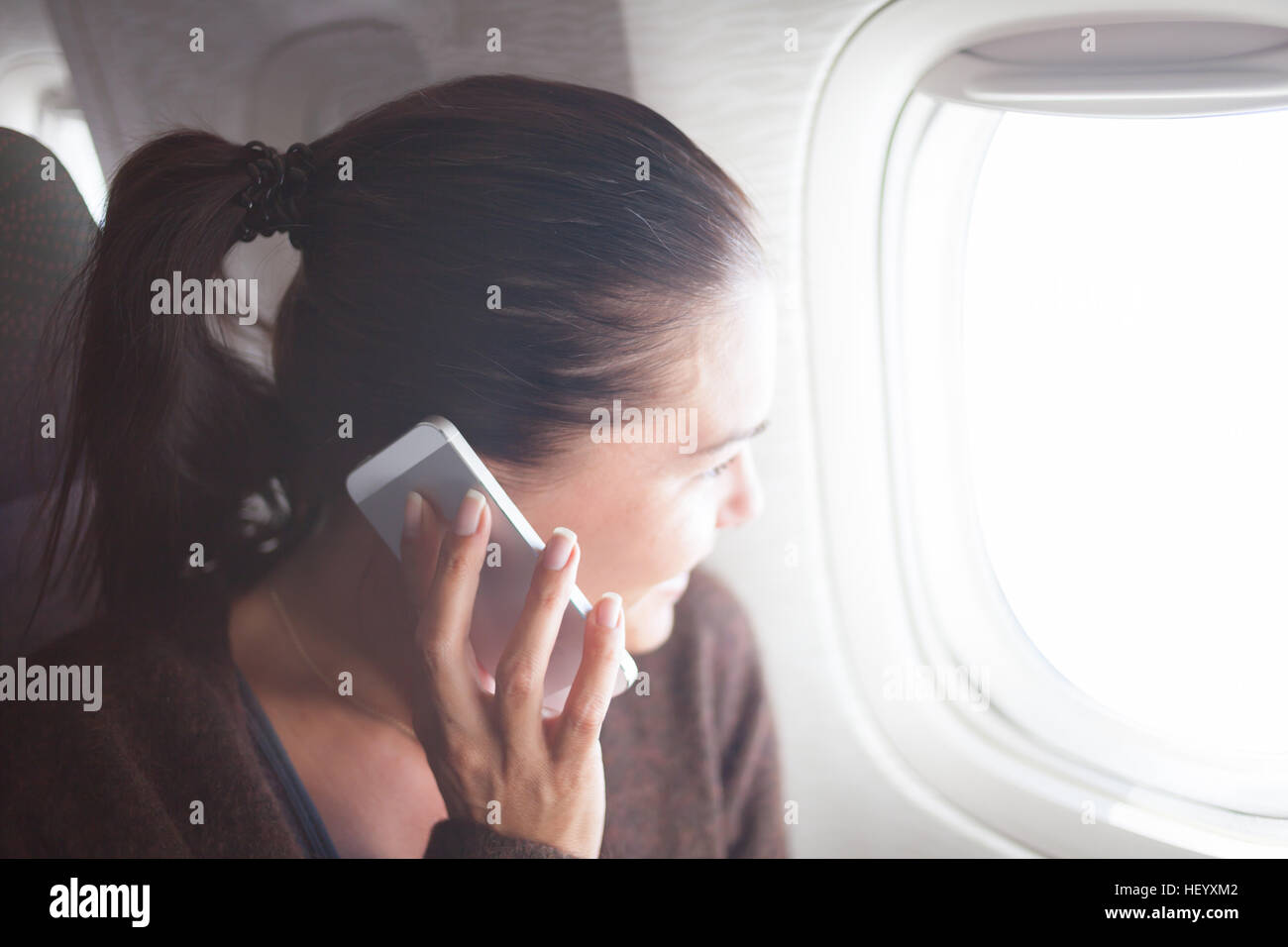 Donna al velivolo con lo smartphone cerca nell'oblò Foto Stock