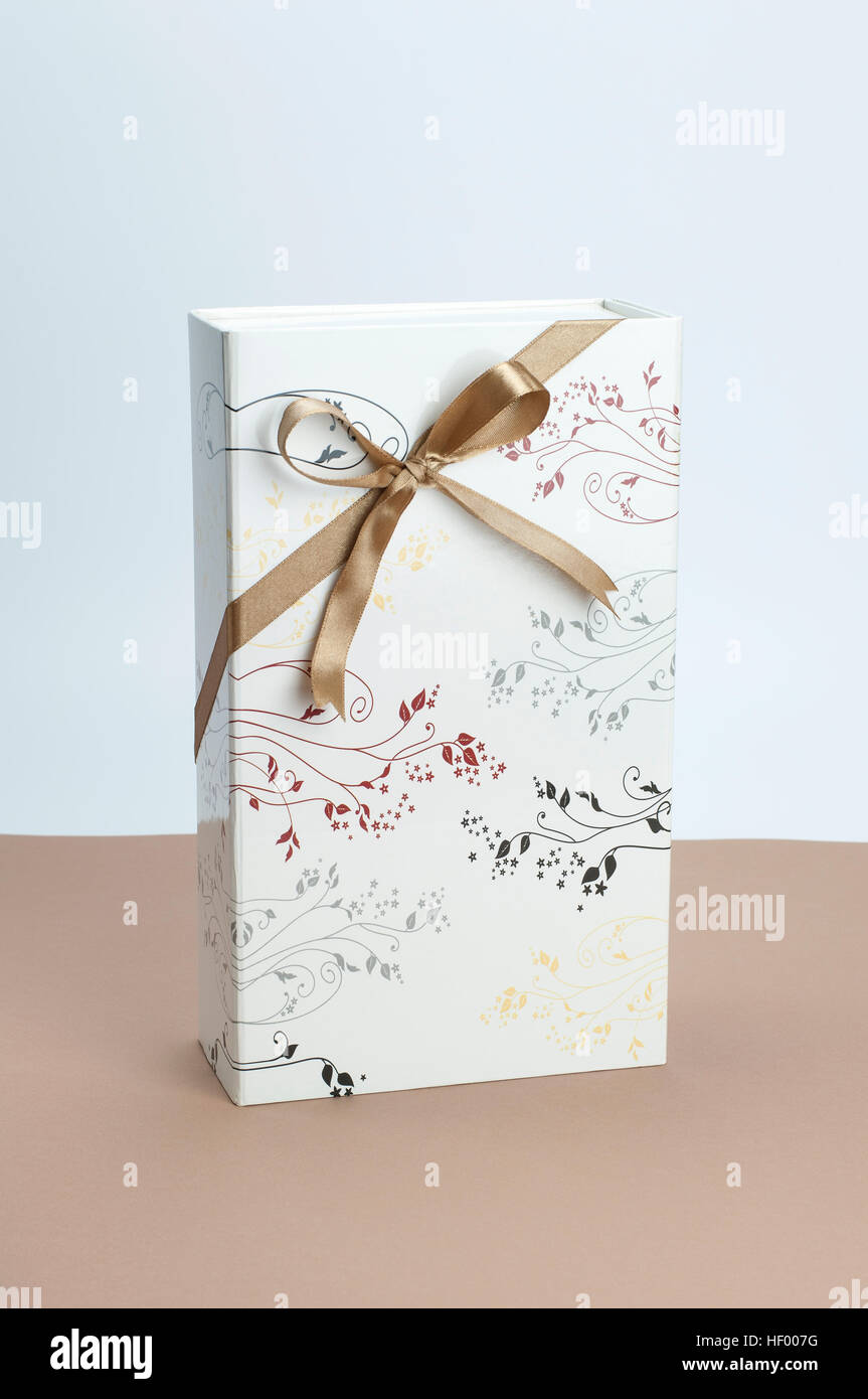 Confezione regalo con nastro dorato sulla prua di marrone chiaro e sfondo bianco. Foto Stock