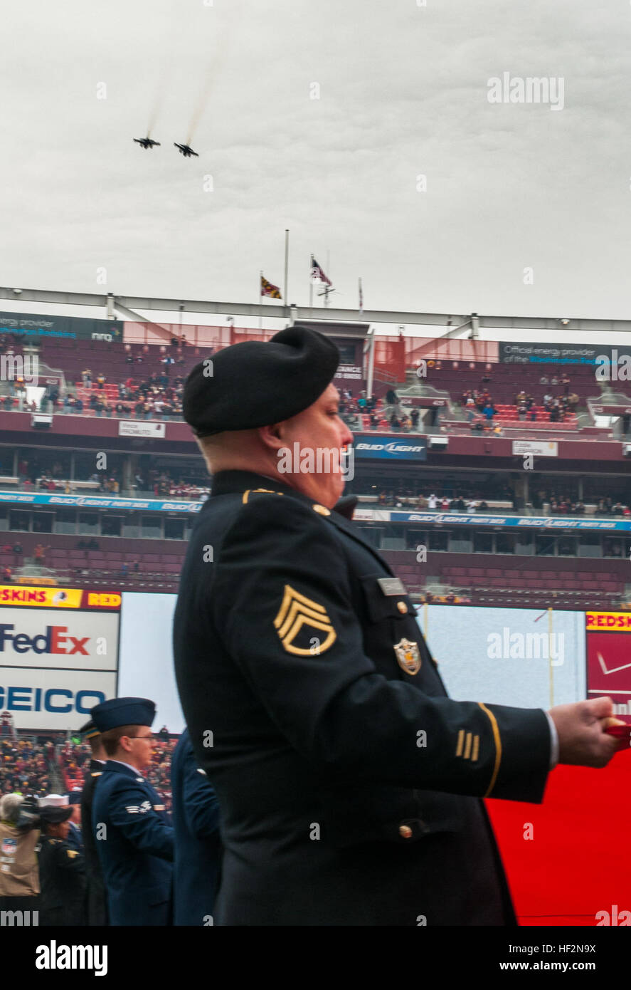 Il personale dell'esercito Sgt. Shannon sostiene il calcio-dimensioni campo bandiera americana mentre due F-16 Fighting Falcon jet da combattimento fuori 113ala, D.C. Air National Guard, Base comune Andrews, volare sul campo di Fedex in Landover, Md., nov. 16, 2014. Il display è stato a sostegno militare di apprezzamento mese dove Washington Redskins riprodotto un saluto al servizio di gioco con top leader eseguendo il coin toss, servizio militare brani riprodotti dal Redskins Band, un 100-cantiere bandiera americana tesa la lunghezza del campo e due F-16s volare alla fine dell'inno nazionale cantato da esercito Sgt. Vicki Golding. (Pho Foto Stock