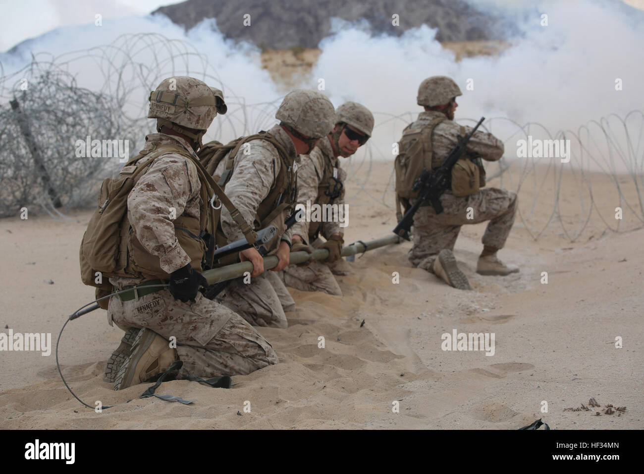 Marines con l'Ingegnere plotone, sede e società di servizio, il combattimento a terra integrati elemento Task Force, elastico M1A2 Bangalores insieme sotto la dissimulazione di fumo per un frettoloso violazione durante un Marine Corps Prova di funzionamento e di attività di valutazione di valutazione alla gamma 107, Marine Corps Air Ground Centro di combattimento ventinove Palms, California, 22 marzo 2015. Da ottobre 2014 a luglio 2015, il GCEITF sarà condotta individuale e collettivo di competenze di livello di formazione in designato il combattimento a terra i bracci di specialità professionali al fine di facilitare la basata su standard di valutazione della perfor fisico Foto Stock