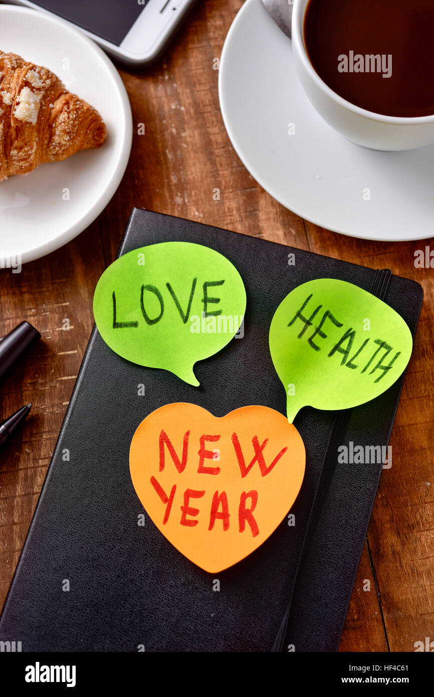 Una nota adesiva con il testo nuovo anno e due più note con le parole di amore e di salute come augurio per il nuovo anno attaccata ad un blocco note su un w Foto Stock