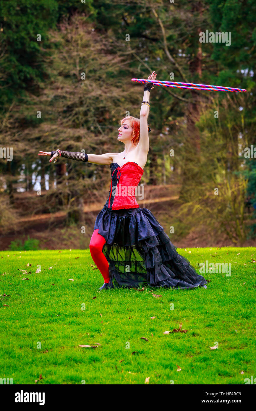 Giovane bella donna in costume di circo gioca con hula hoop nel parco. Foto Stock