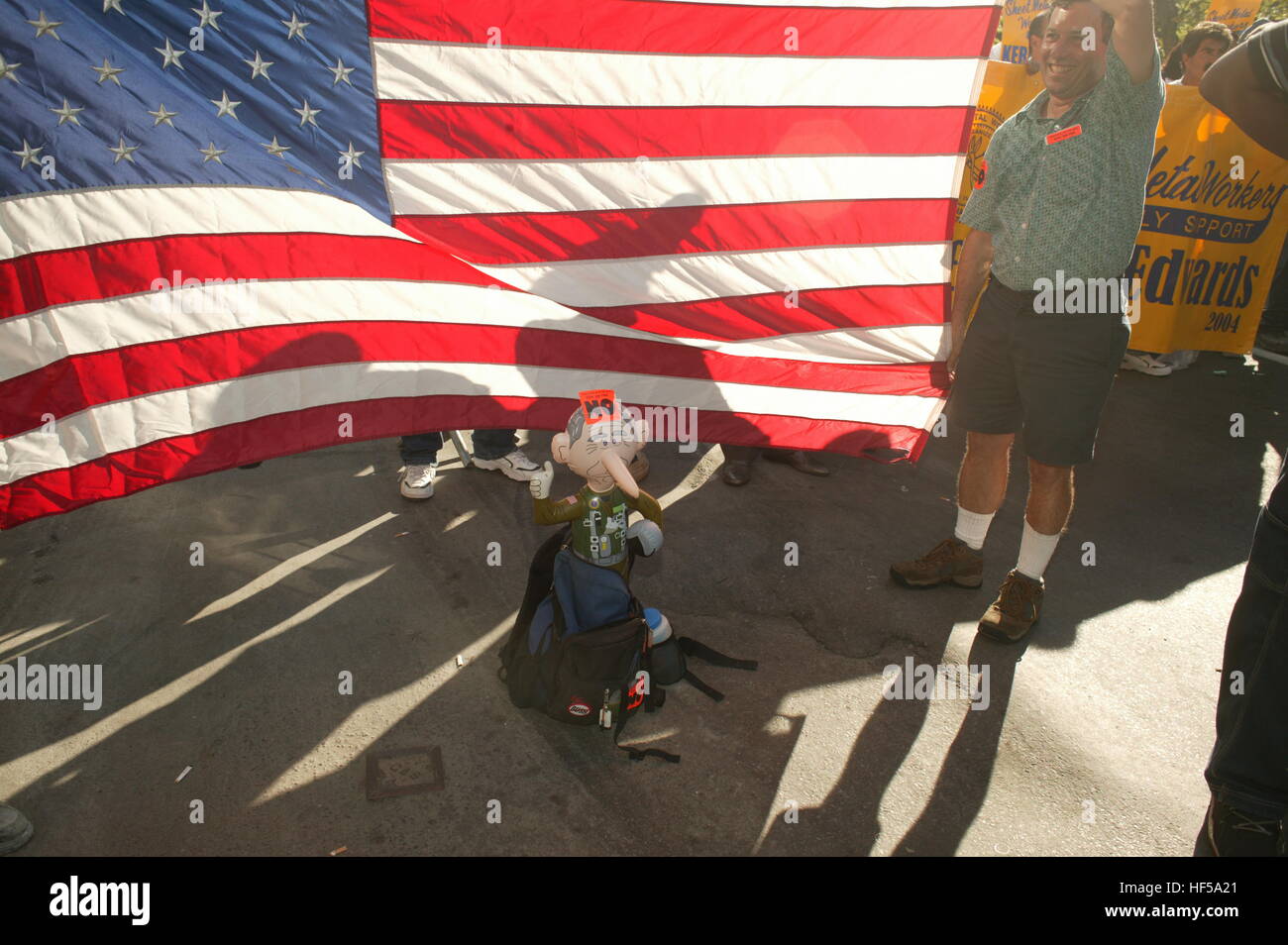 Manifestanti sostare nelle vicinanze di una bandiera americana con un Blow up dollar di George W. Bush come un pilota in riferimento al suo atterraggio su un air craft portante in un uniforme da pilota dicendo, "missione compiuta,' per dichiarare la guerra in Iraq ha vinto. I manifestanti hanno protestato durante il 2004 Convention Nazionale Repubblicana. Le truppe americane non lasciare il Iraq fino al 2011. Foto Stock