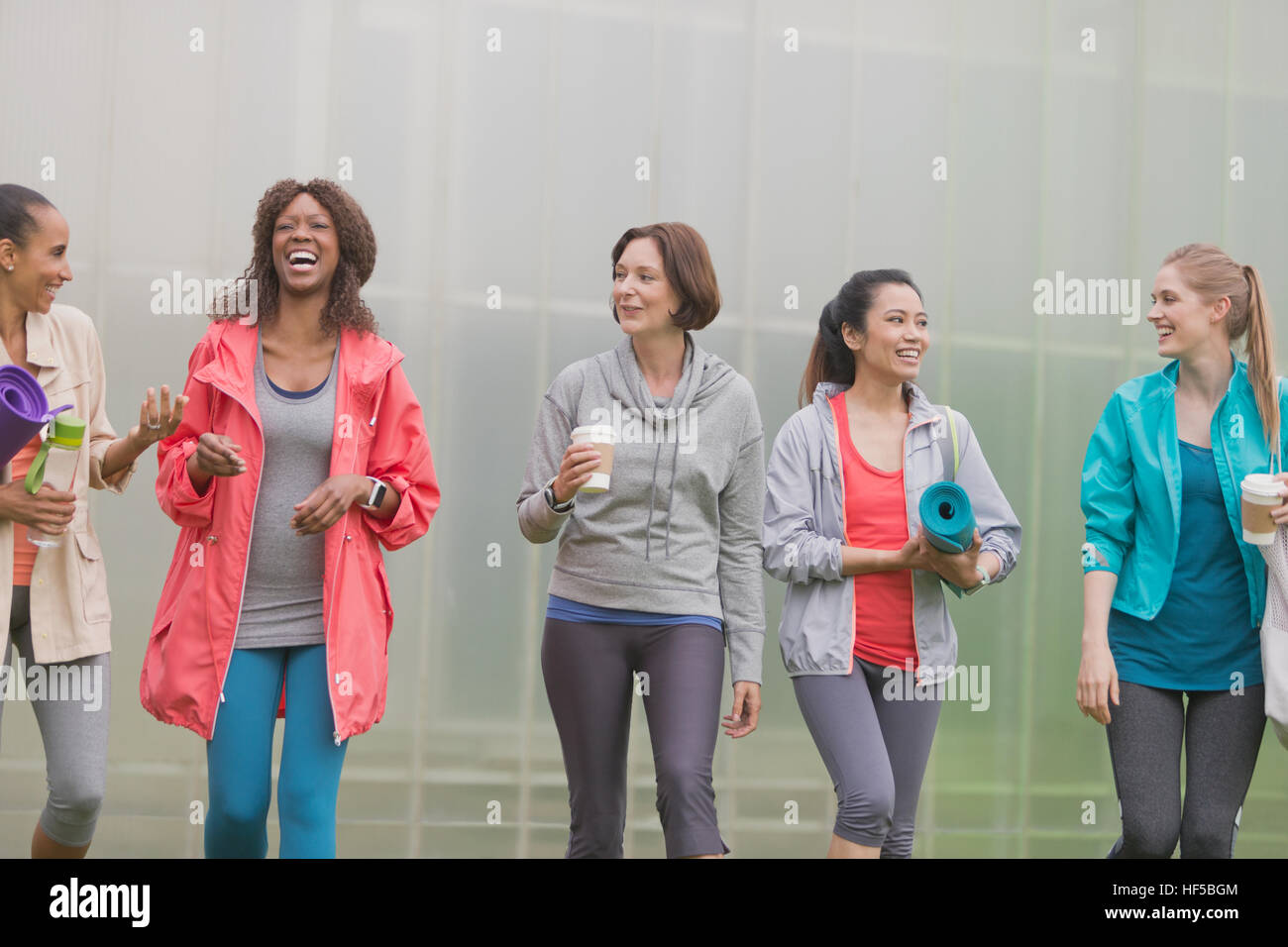 Donna sorridente camminando con Materassini da yoga e caffè Foto Stock