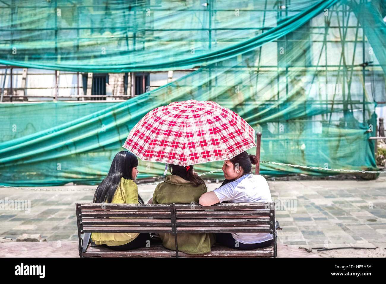 Tre giovani donne che condividono un ombrello in una giornata intensa a Hanuman Dhoka, Durbar Square, Kathmandu. Foto Stock