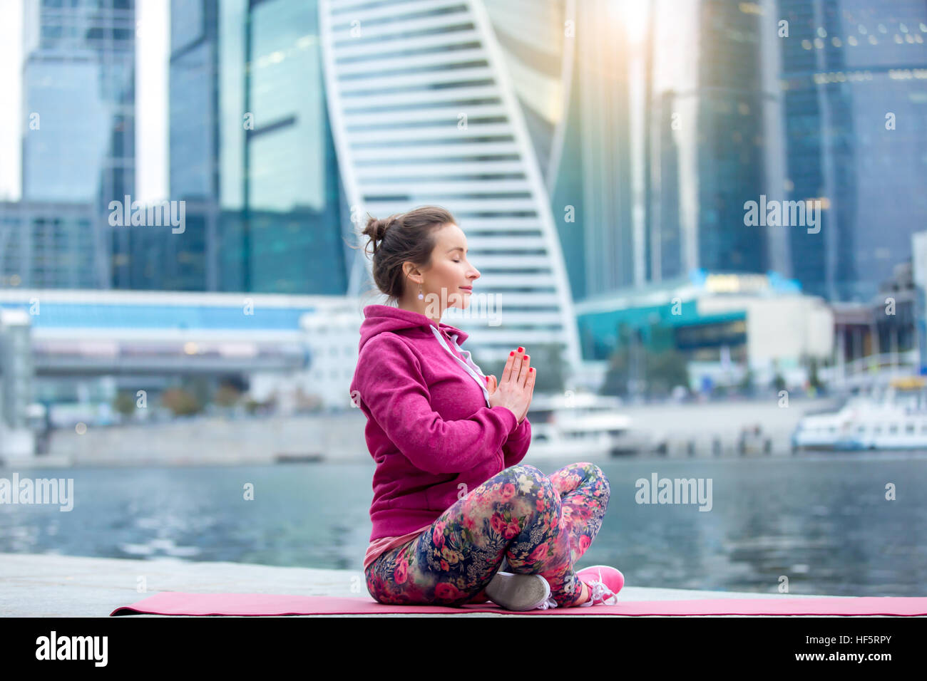 Giovane donna in sede di facile posa contro la città e il fiume Foto Stock