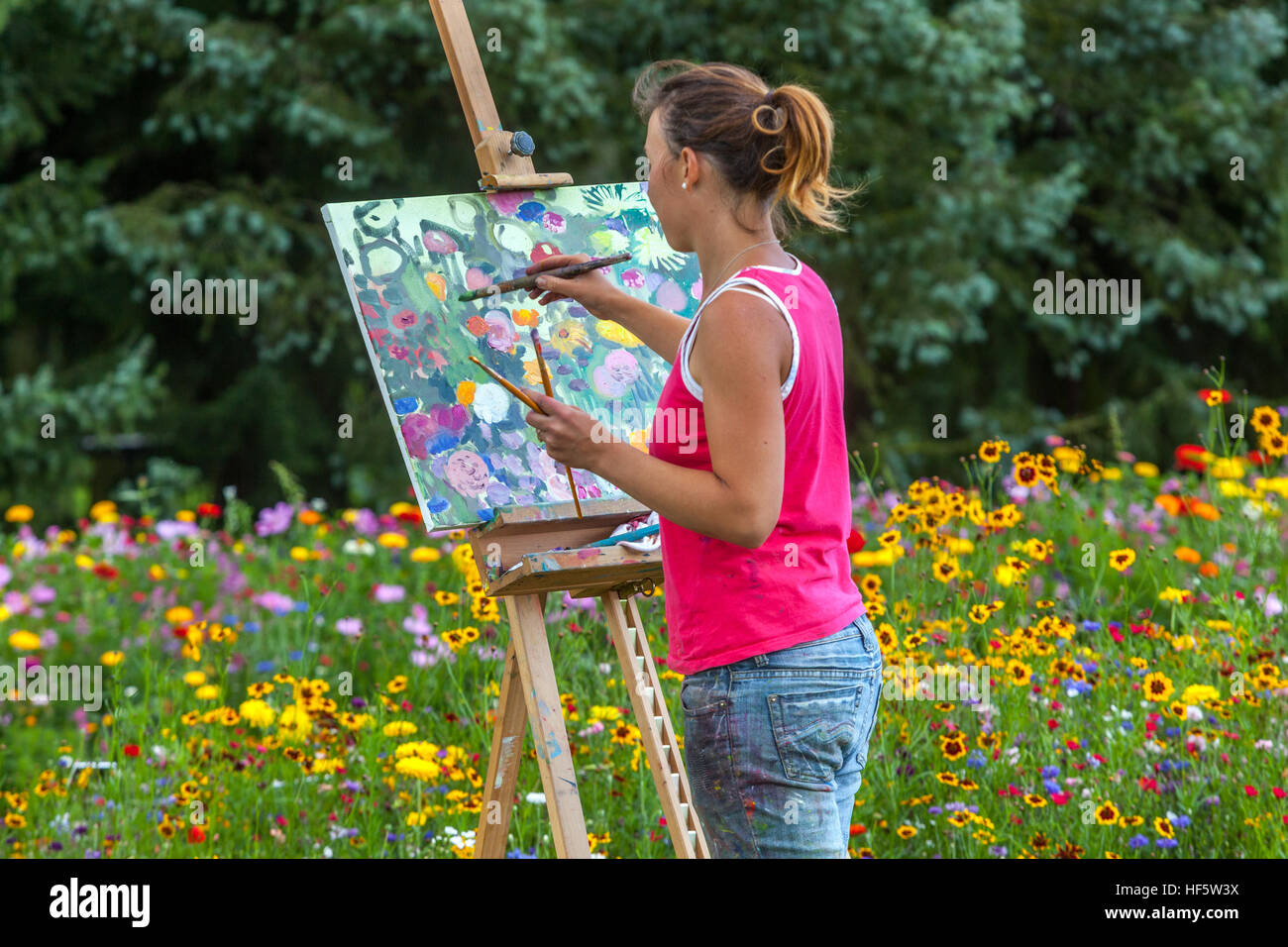 Una donna che dipinge fiori un quadro in un giardino colorato attività di svago donna che dipinge tela vista posteriore Foto Stock