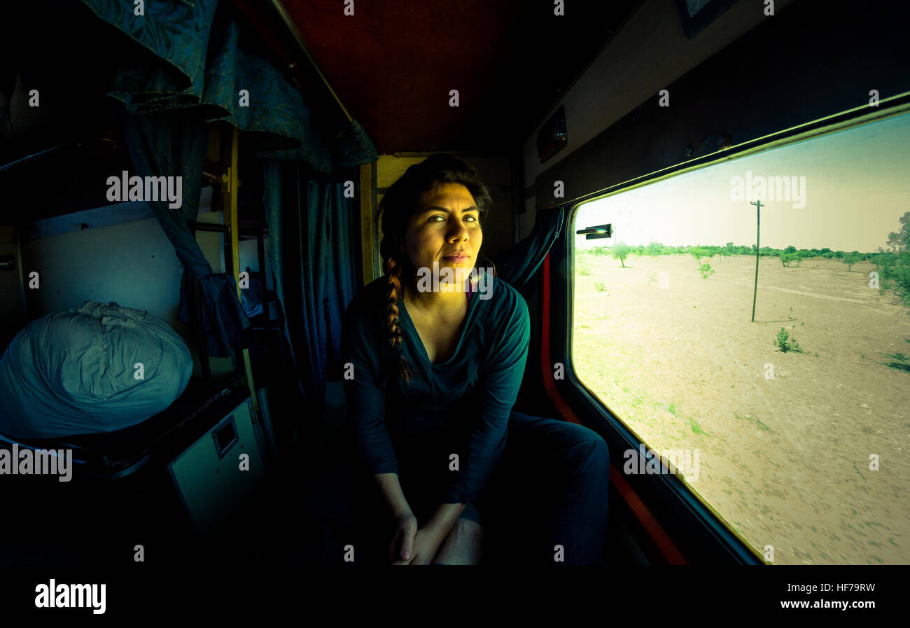 Una giovane donna su un solitario cammino attraverso il deserto del Rajasthan, guarda il mondo dalla finestra del treno. Foto Stock