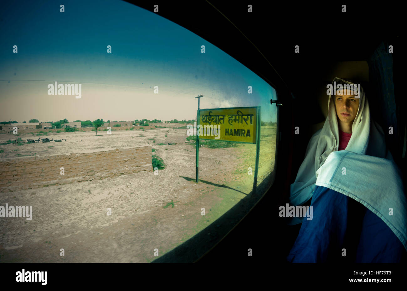 Un giovane uomo su un solitario cammino attraverso il deserto del Rajasthan, guarda il mondo dalla finestra del treno. Foto Stock