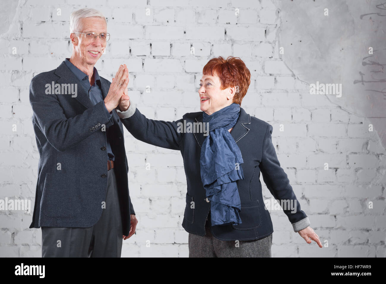 Dare un alto cinque. Sorridenti vecchia coppia piedi cuddling insieme isolato su bianco Sfondo mattone. copia di spazio. Foto Stock