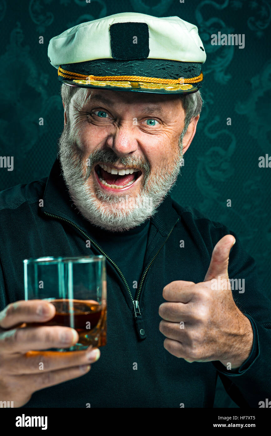 Ritratto di vecchio marinaio uomo come capitano a maglione nero e hat bere cognac nero su sfondo per studio Foto Stock