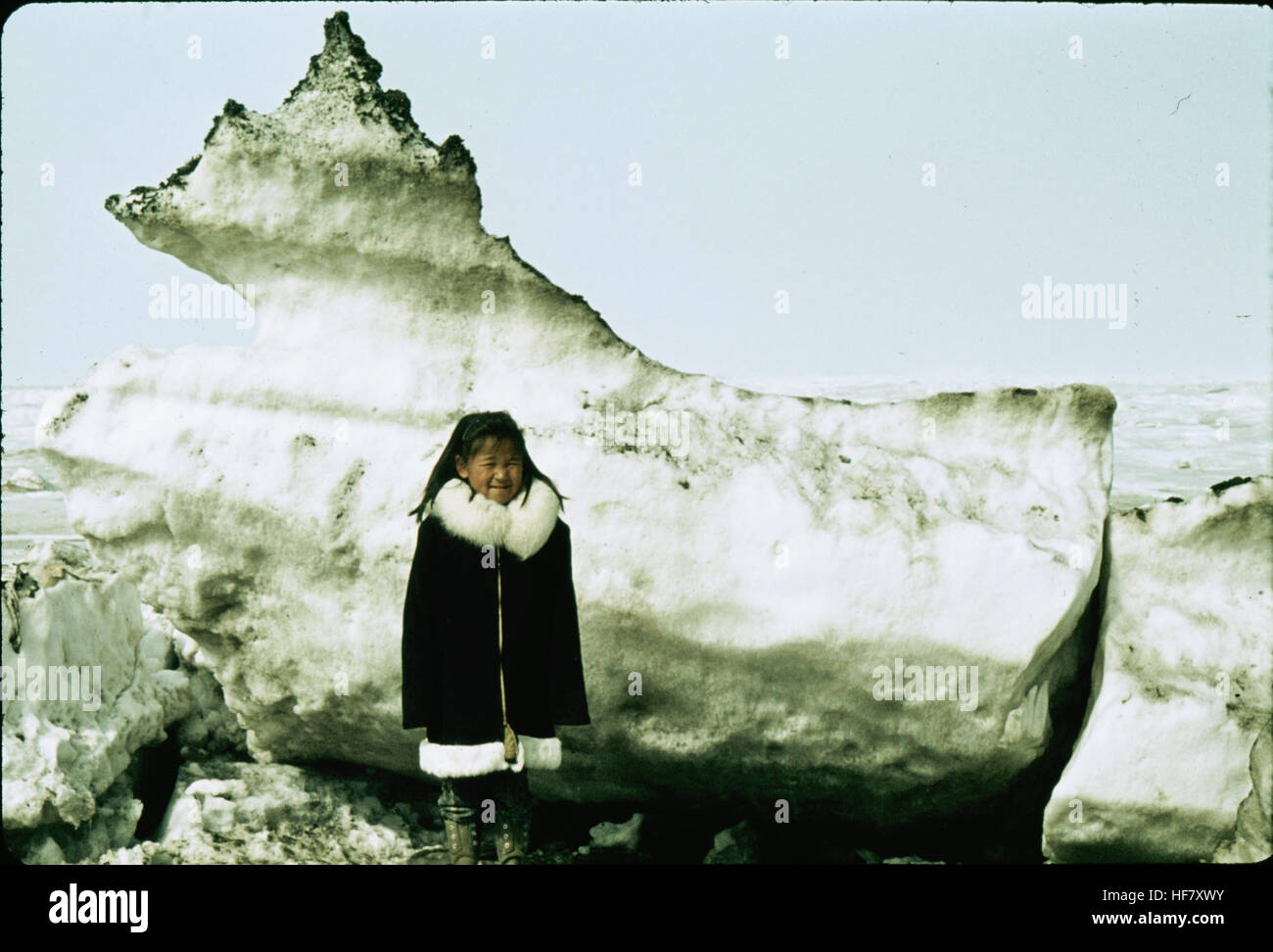 Una fotografia di un bambino eschimese in piedi di fronte a un grande blocco di ghiaccio, scattata a Point Barrow, Alaska, che cattura l'ambiente duro e ghiacciato della regione. Foto Stock