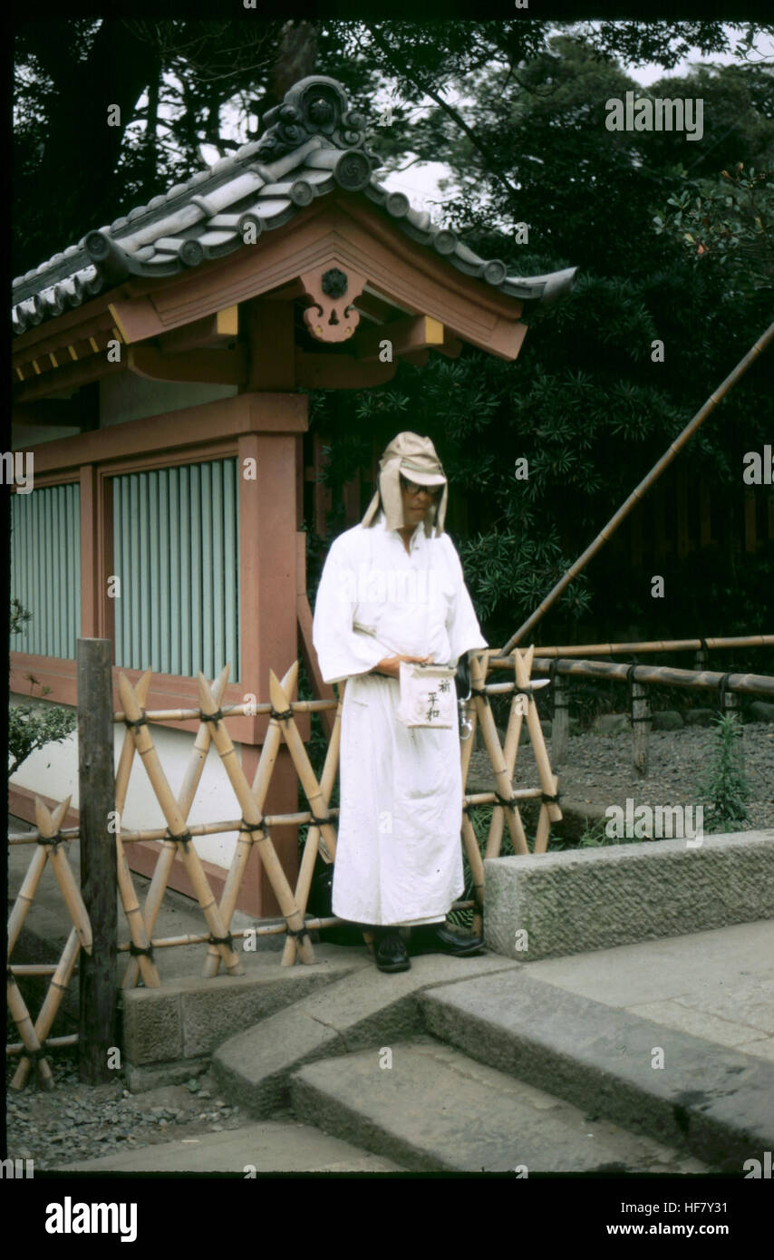 Una fotografia che mostra un mendicante vicino a un complesso di templi a Kamakura, Isola di Honshu, Giappone, che riflette il contrasto tra siti religiosi e povertà nel Giappone dell'inizio del XX secolo. Foto Stock