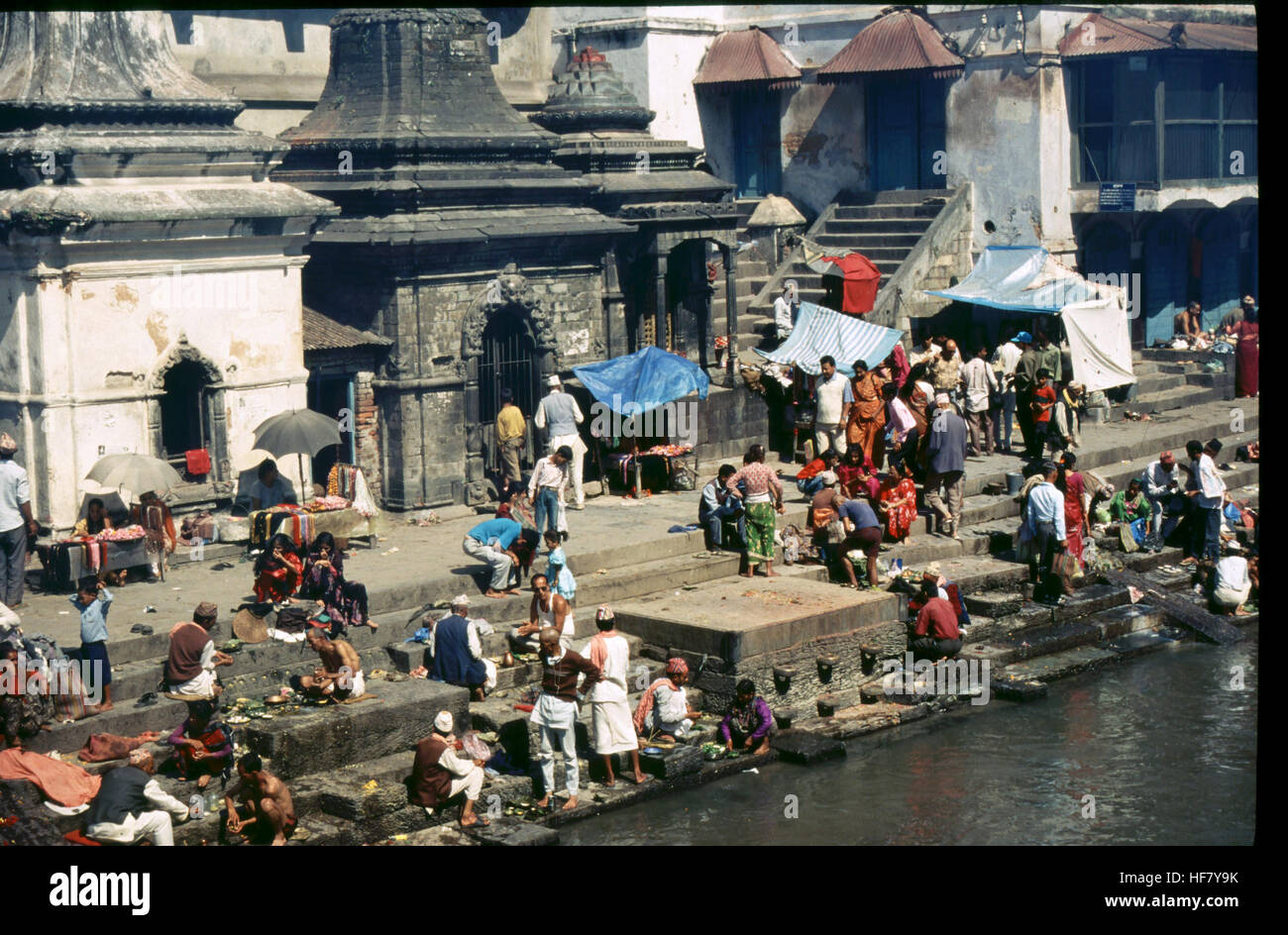 Questa immagine cattura le persone nei ghat del fiume Bagmati vicino a Pashupatinath, Nepal. Pashupatinath, conosciuta come "piccola Benares", è un importante sito di pellegrinaggio indù, rinomato per il suo significato religioso e la sua bellezza architettonica. Foto Stock