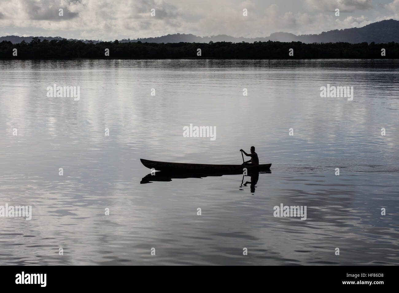 Un pescatore pagaie sua piroga in acqua calma tra isole remote e nelle Isole Salomone. Foto Stock